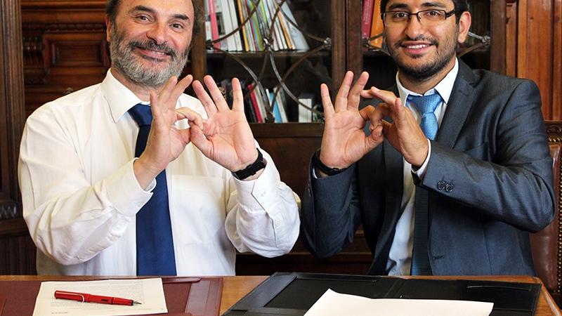 Los representantes de las instituciones firmantes, el director de la DIBAM, Ángel Cabeza Monteira, junto a Rodrigo Campos Muñoz, (Fundación AMOMA) dicen gracias en lenguaje de señas.