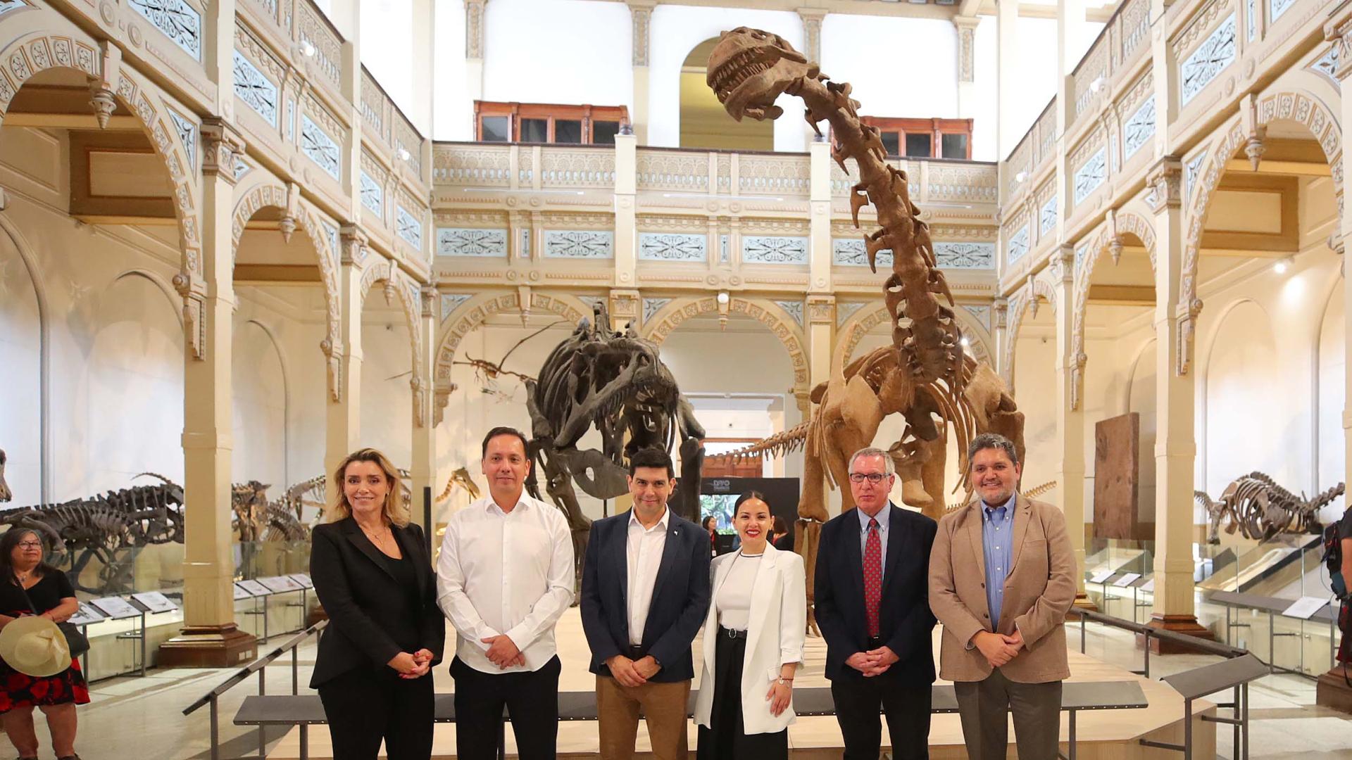 Autoridades en el hall central del museo posan junto a dos esqueletos de dinosaurios