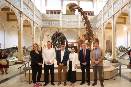 Autoridades en el hall central del museo posan junto a dos esqueletos de dinosaurios